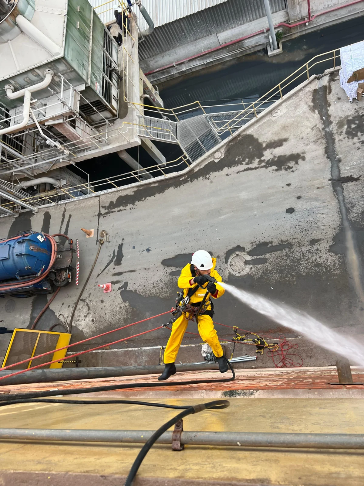 Alpinista industrial executando limpeza de alta pressão com equipamentos de proteção