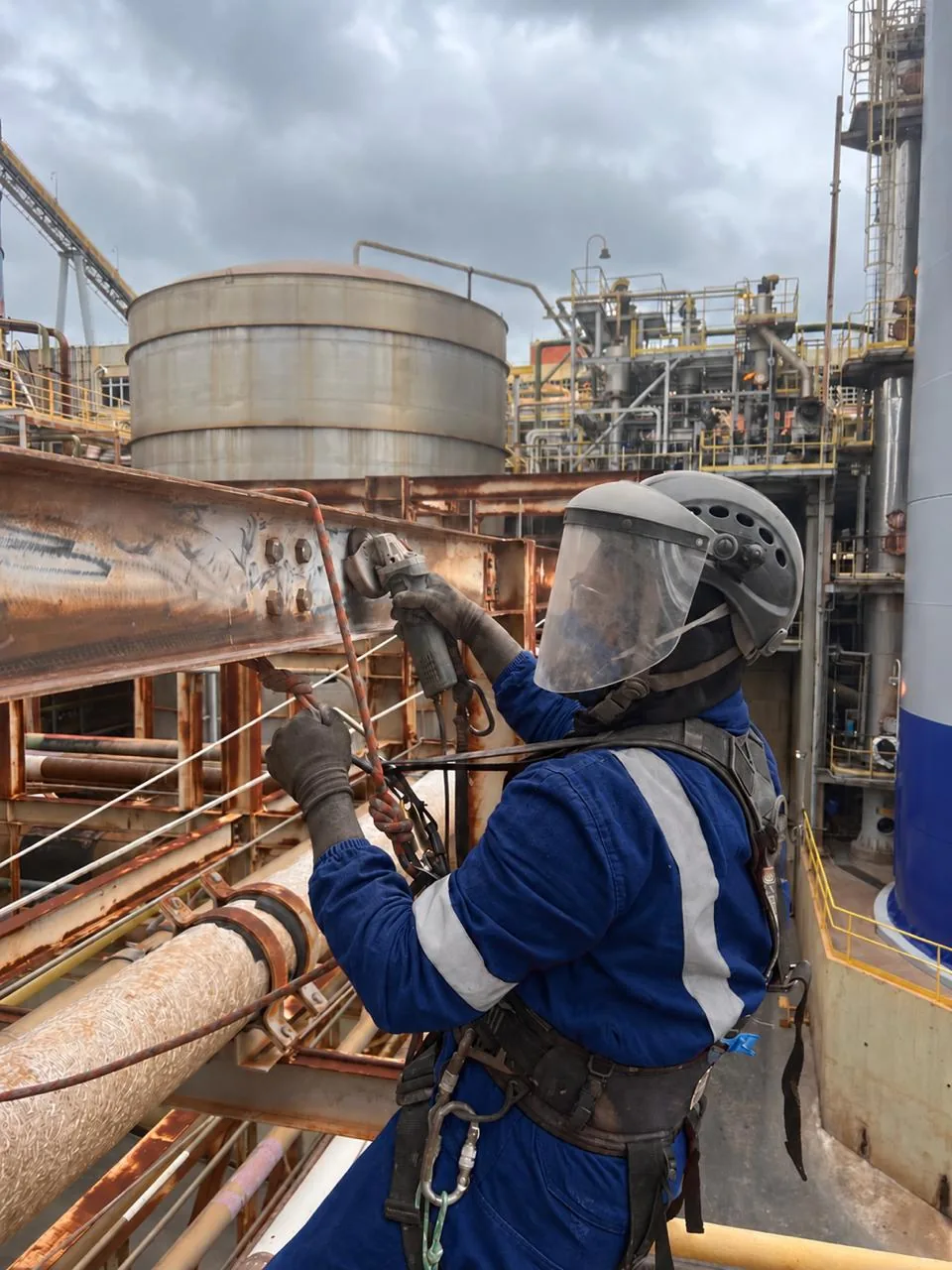 Profissional em acesso por cordas com esmerilhadeira trabalhando em viga metálica em instalação industrial